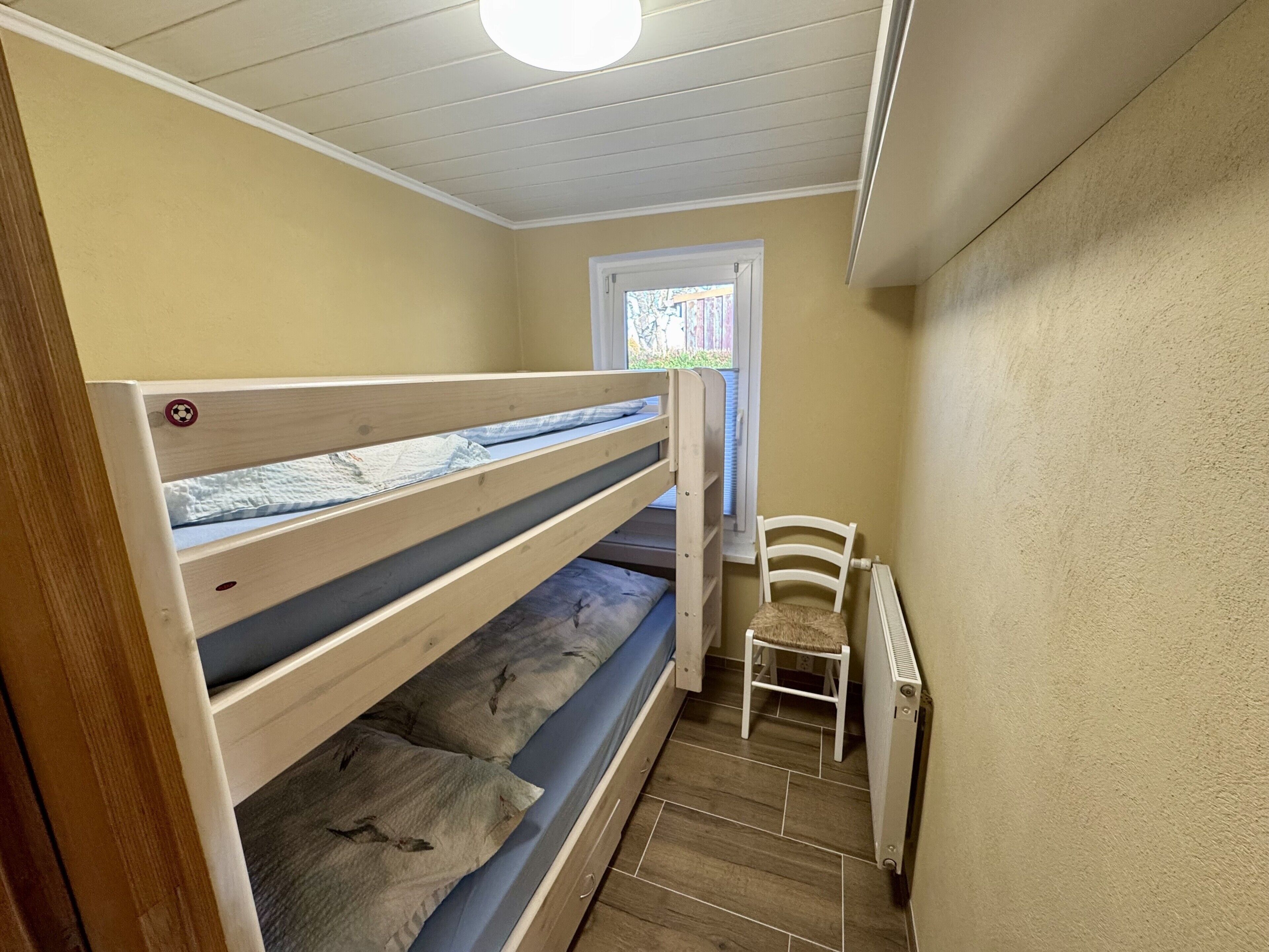 Ein Etagenbett mit Fenster, Stuhl und Heizkörper.