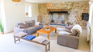 A living room with a stone wall, a fireplace, a sofa, a coffee table, and a bench. - Charming villa with heated pool • Sainte-Marine - Village and beaches on foot (Combrit)