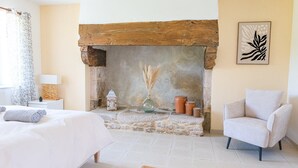 A bedroom with a stone fireplace, a bed, a chair, and a wall-mounted artwork. - Charming villa with heated pool • Sainte-Marine - Village and beaches on foot (Combrit)