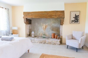 A bedroom with a stone fireplace, a bed, a chair, and a wall-mounted artwork.