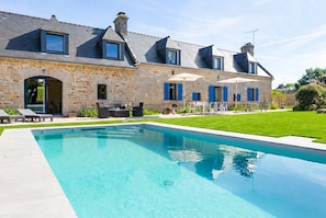A stone house with a swimming pool, outdoor seating, and a well-maintained lawn.