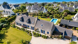An aerial view of a coastal residential area with houses, a swimming pool, and a clear view of the sea. - Charming villa with heated pool • Sainte-Marine - Village and beaches on foot (Combrit)