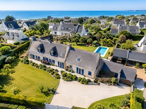 An aerial view of a coastal residential area with houses, a swimming pool, and a clear view of the sea.