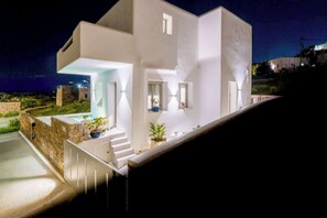 Un edificio moderno blanco con una escalera que conduce a un área exterior cubierta, rodeado de vegetación.
