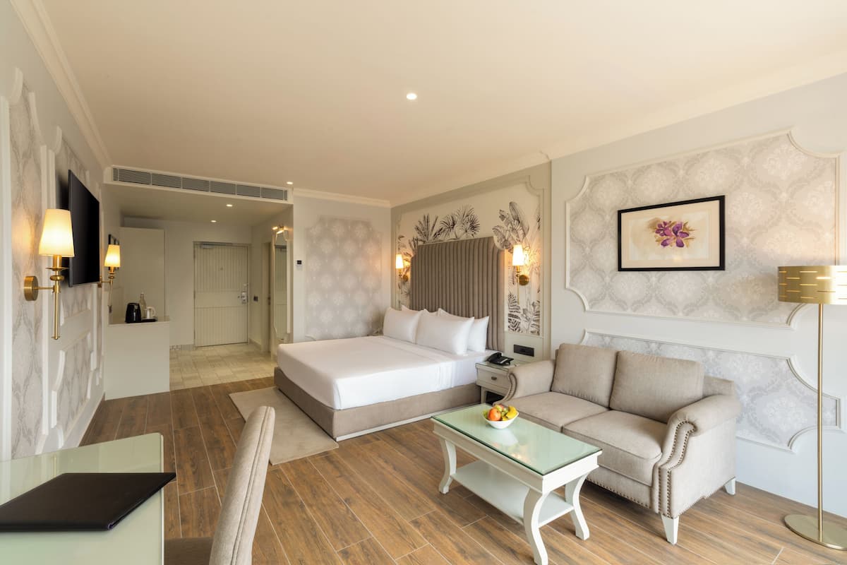A hotel room with a bed, a sofa, a glass table with fruit, a desk, and a TV.