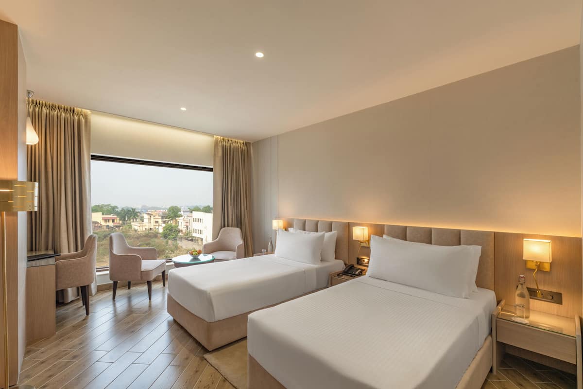 A hotel room with two beds, a desk, a chair, and a view of the city.