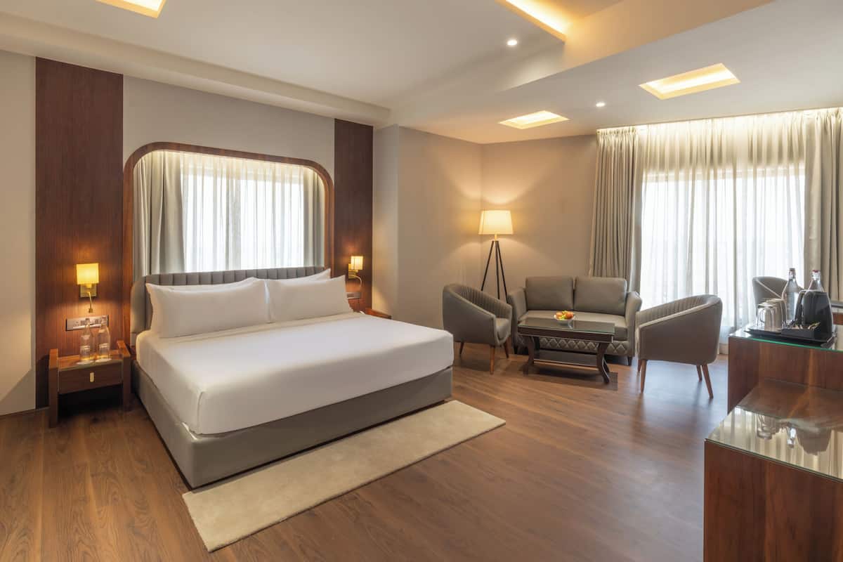A hotel room with a large bed, a desk with a chair, a sofa, a floor lamp, and a coffee table.
