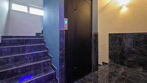 Eine moderne Treppe mit dunklen Marmorstufen und -wänden, die zu einem schwarzen Aufzug führt.