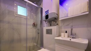 Ein modernes Badezimmer mit einer gläsernen Duschkabine, Toilette, Waschbecken mit Wasserhahn und Toilettenpapierhalter.