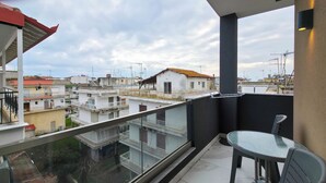 Ein Balkon mit Glastisch und Stühlen, mit Blick auf ein Wohngebiet mit mehreren Gebäuden.