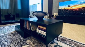 Un salon moderne doté d’un grand téléviseur à écran plat, d’un meuble noir contenant des livres et d’un tapis à motifs.