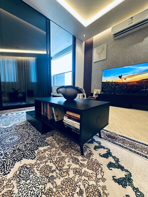 A modern living room with a large flat-screen TV, a black entertainment unit with books, and a patterned rug. - LP78- 2-bedroom apartment in marvelous Riyadh with cool AC (Riyadh)