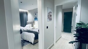 Un couloir d’hôtel avec un lit en arrière-plan, une plante en pot et une porte donnant sur une autre pièce.