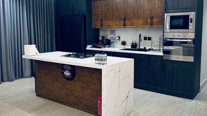 Une cuisine moderne avec des meubles en bois foncé, un îlot central en marbre blanc, des appareils électroménagers en acier inoxydable et un rideau gris en arrière-plan.