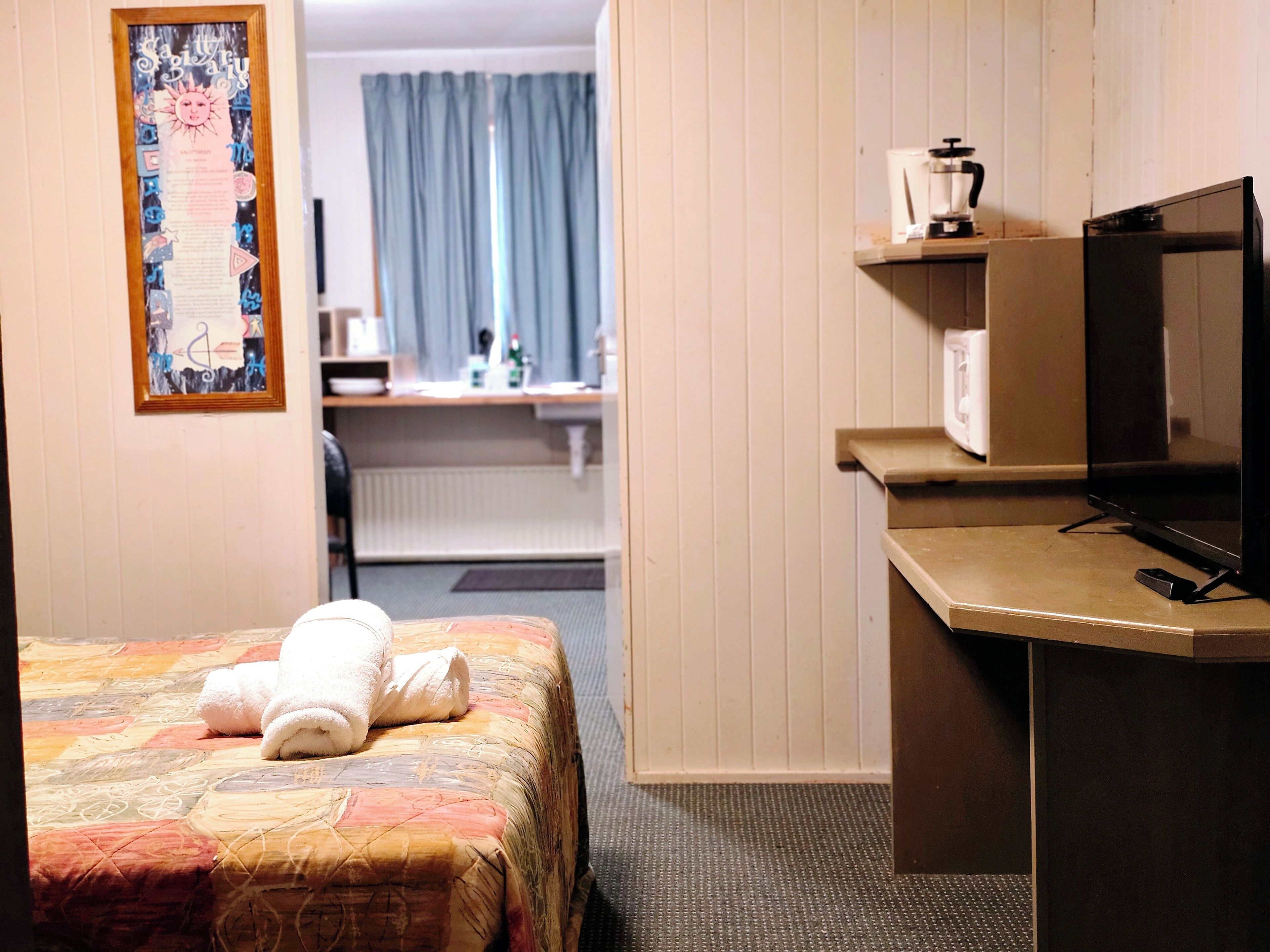 A hotel room with a bed, a desk with a television, a coffee maker, and a framed picture on the wall.