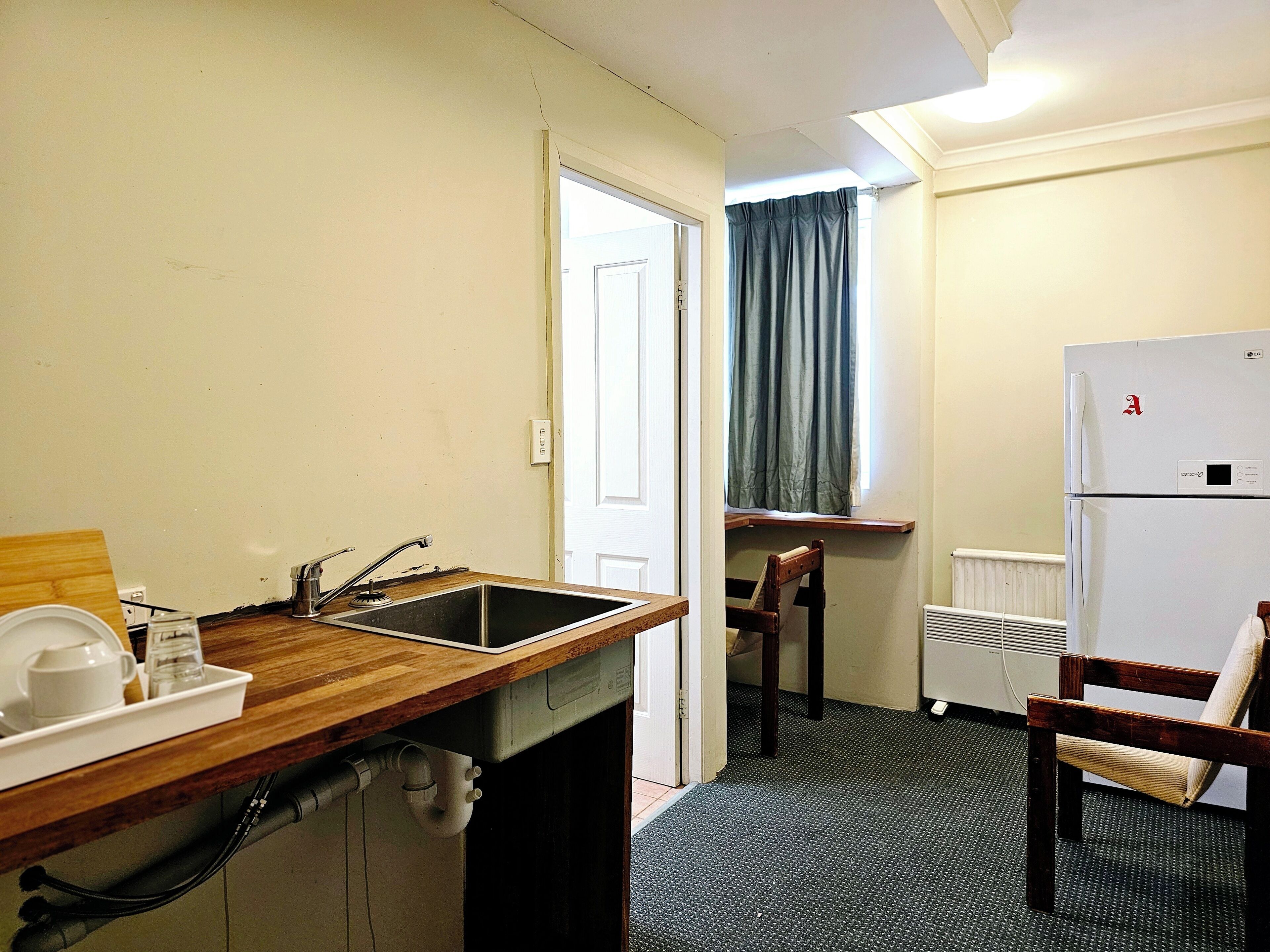 Une cuisine compacte comprenant un évier, un plan de travail en bois, une chaise et un réfrigérateur blanc.