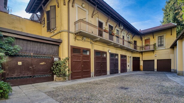 En byggnad med flera garageportar, en balkong och en grusbelagd innergård.