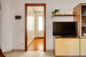 A room with a TV on a cabinet, a wooden door leading to another room, and a plant on a shelf. - Hostmate - Milano - Plinio - Città Studi (Milano)