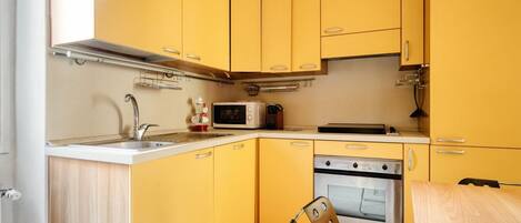 A kitchen with yellow cabinets, a stainless steel sink, a microwave, and an oven.