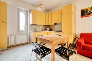 A compact kitchen with yellow cabinets, a wooden table, and black chairs. - Hostmate - Milano - Plinio - Città Studi (Milano)