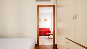 Ett hotellrum med en säng, en garderob, en dörr som leder till ett annat rum och en röd soffa.