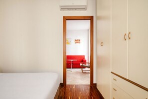 A hotel room with a bed, a wardrobe, a door leading to another room, and a red sofa. - Hostmate - Milano - Plinio - Città Studi (Milano)