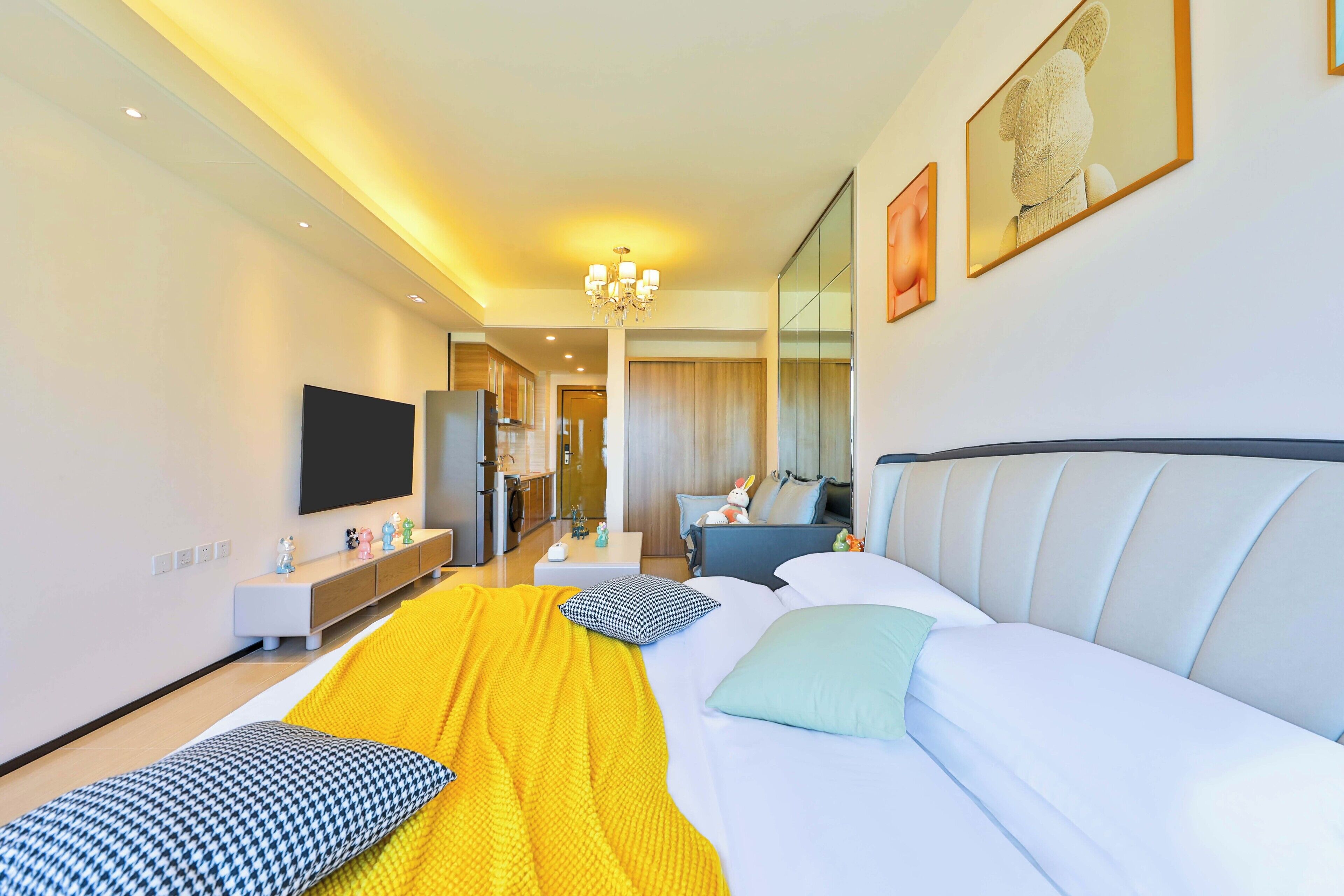 A modern hotel room with a large bed, a TV, a desk, and a bathroom visible in the background.