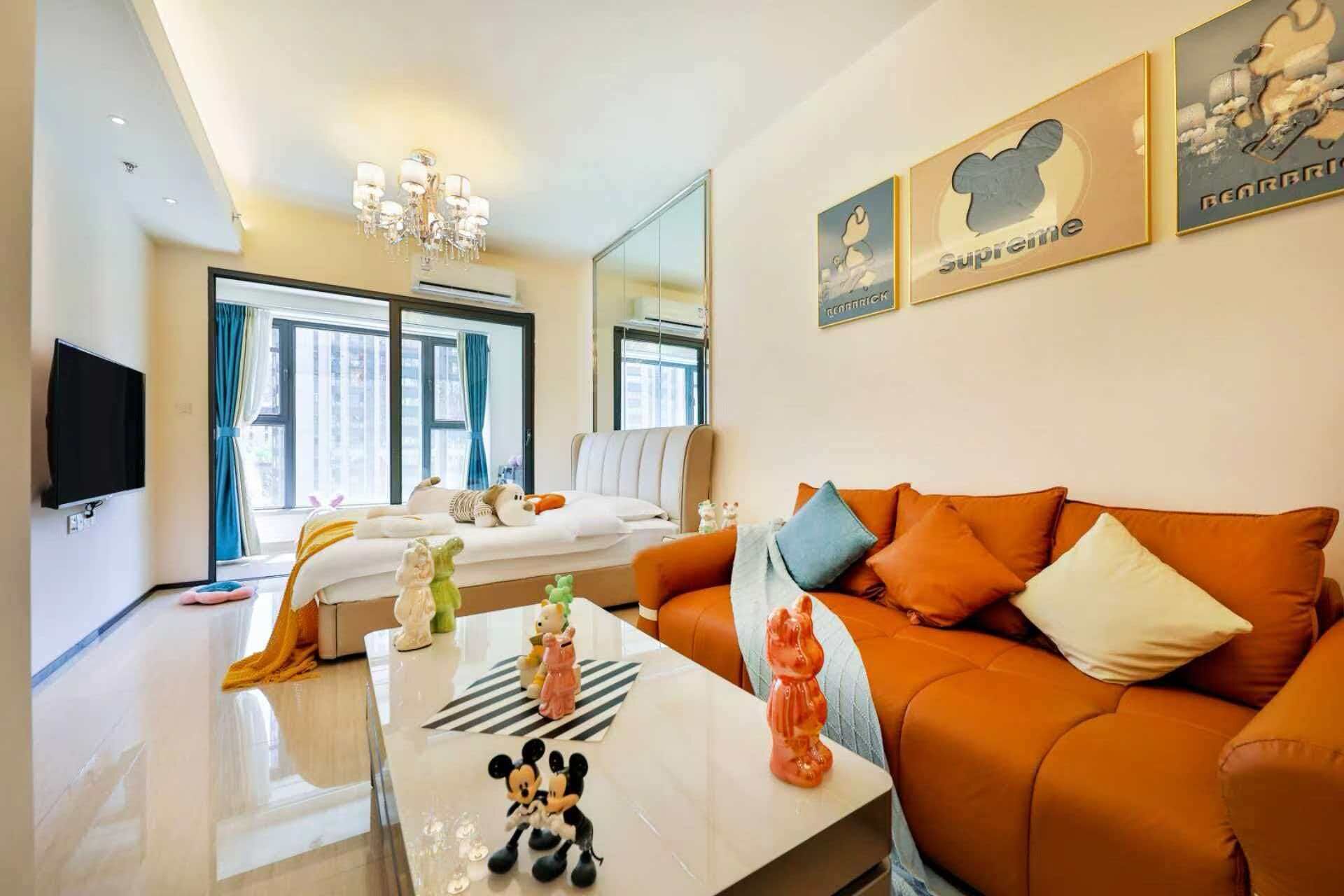 A modern hotel room with a large bed, a sofa, a flat-screen TV, and a chandelier.