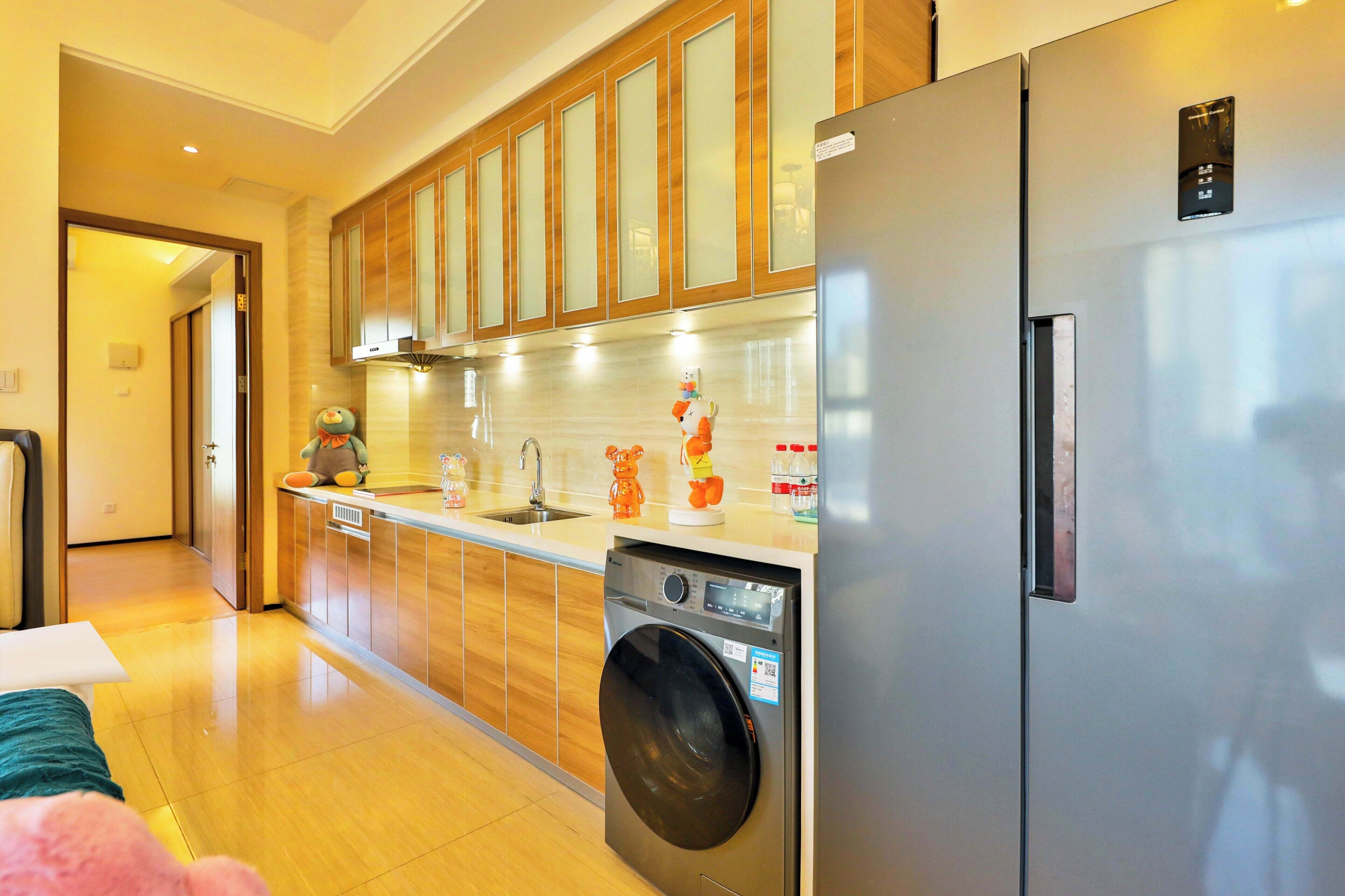 A modern kitchen with wooden cabinets, a stainless steel refrigerator, a washing machine, and a sink.