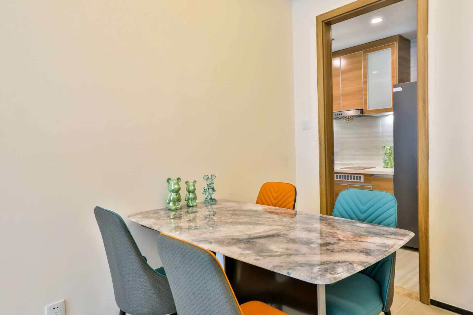 Un comedor con una mesa de mármol, dos sillas y una cocina visible a través de una puerta abierta.