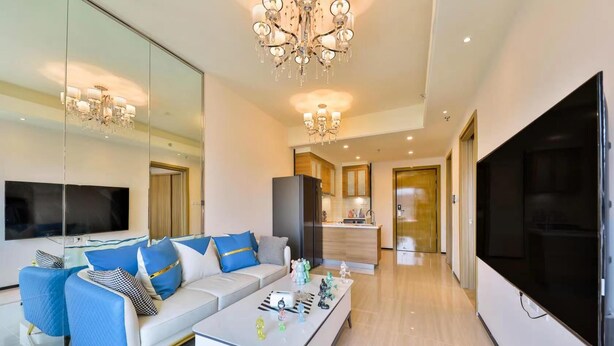 Una sala de estar moderna con sofá, mesa de centro y televisor. Hay una zona de cocina con armarios y un refrigerador.