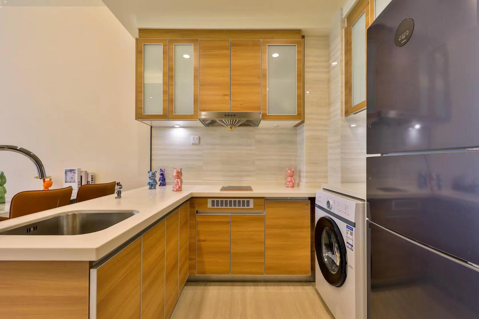A modern kitchen with wooden cabinets, a stainless steel sink, a built-in washing machine, and a large refrigerator.
