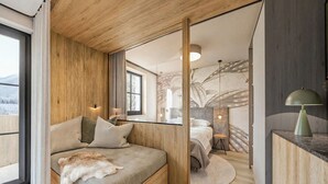A modern bedroom with a wooden ceiling, a large bed with a fur throw, a desk with a lamp, and a view of a snowy landscape through a window. - Apartment mit 1 Schlafzimmer (Kaprun)