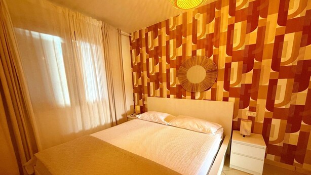 A hotel room with a bed, curtains, a bedside table, and a patterned wall. - Apartment with premium amenities, Rosolina (Rosolina)