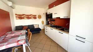 A compact kitchen with white cabinets, a dining table, and a sofa. - Apartment with premium amenities, Rosolina (Rosolina)