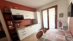 A compact kitchen with white cabinets, a gas stove, and a dining area with a patterned tablecloth. - Apartment with premium amenities, Rosolina (Rosolina)