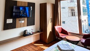 A hotel room with a television, wardrobe, seating area, and a view through a window. - The Manthan Heights (Vrindavan)