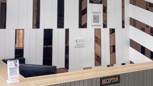 A reception desk with a check-out time sign, a QR code for digital check-in, and a reception area with a modern design. - The Manthan Heights (Vrindavan)