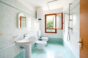 A bathroom with a sink, two toilets, a shower, and a window with a view of greenery. - Holiday Getaway for 5 near the Beach (Rosolina Mare RO)