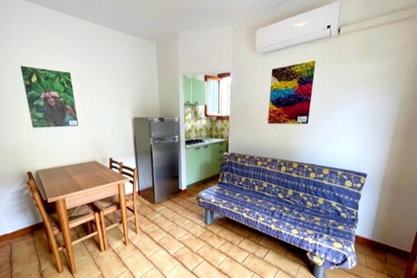A small, compact living space with a wooden dining table and chairs, a sofa, and a kitchenette in the background. - Holiday Getaway for 5 near the Beach (Rosolina Mare RO)