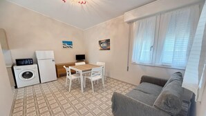 A compact living space with a kitchenette, a dining area, a sofa, and a washing machine. - Rosolina Apartment Near Porto Caleri (Rosolina Mare RO)