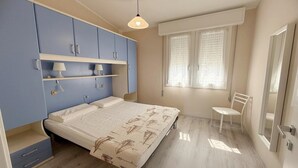 A bedroom with a bed, a chair, a window with blinds, and a wardrobe. - Rosolina Apartment Near Porto Caleri (Rosolina Mare RO)