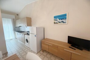 A compact kitchen with a washing machine, a refrigerator, and a wooden cabinet. - Rosolina Apartment Near Porto Caleri (Rosolina Mare RO)