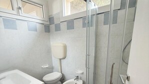 A bathroom with a glass-enclosed shower, a sink, and two toilets. - Rosolina Apartment Near Porto Caleri (Rosolina Mare RO)