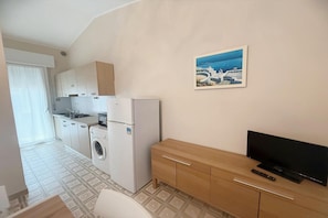 Eine kleine Küche mit Waschmaschine, Kühlschrank und Holzschrank.