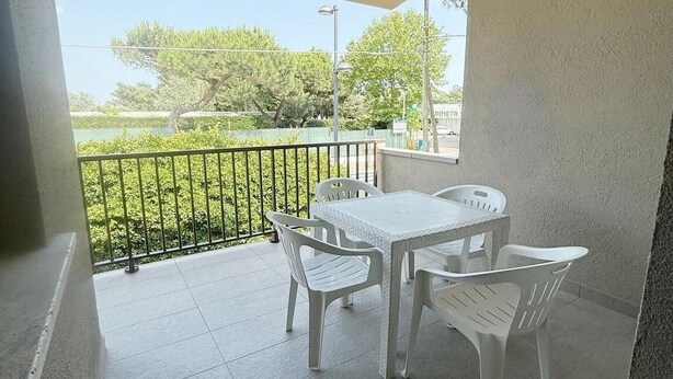Un balcó amb taula i cadires, vista d'arbres i un edifici al fons.