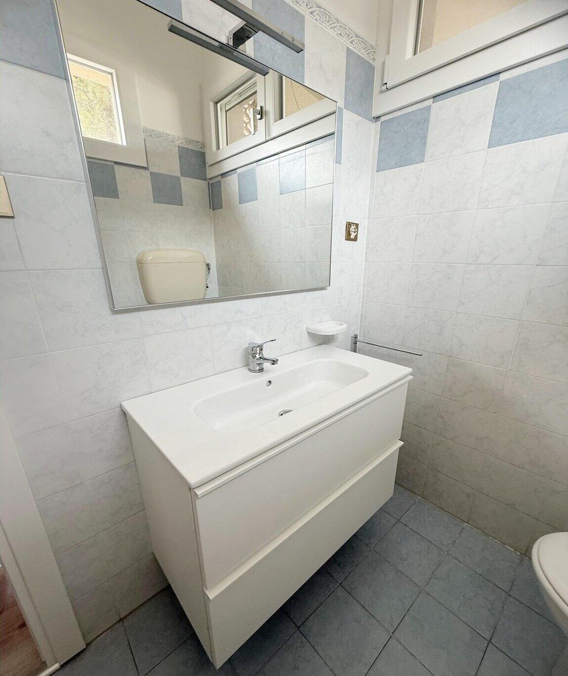 Een badkamer met een wit wastafelmeubel, spiegel en betegelde wanden.