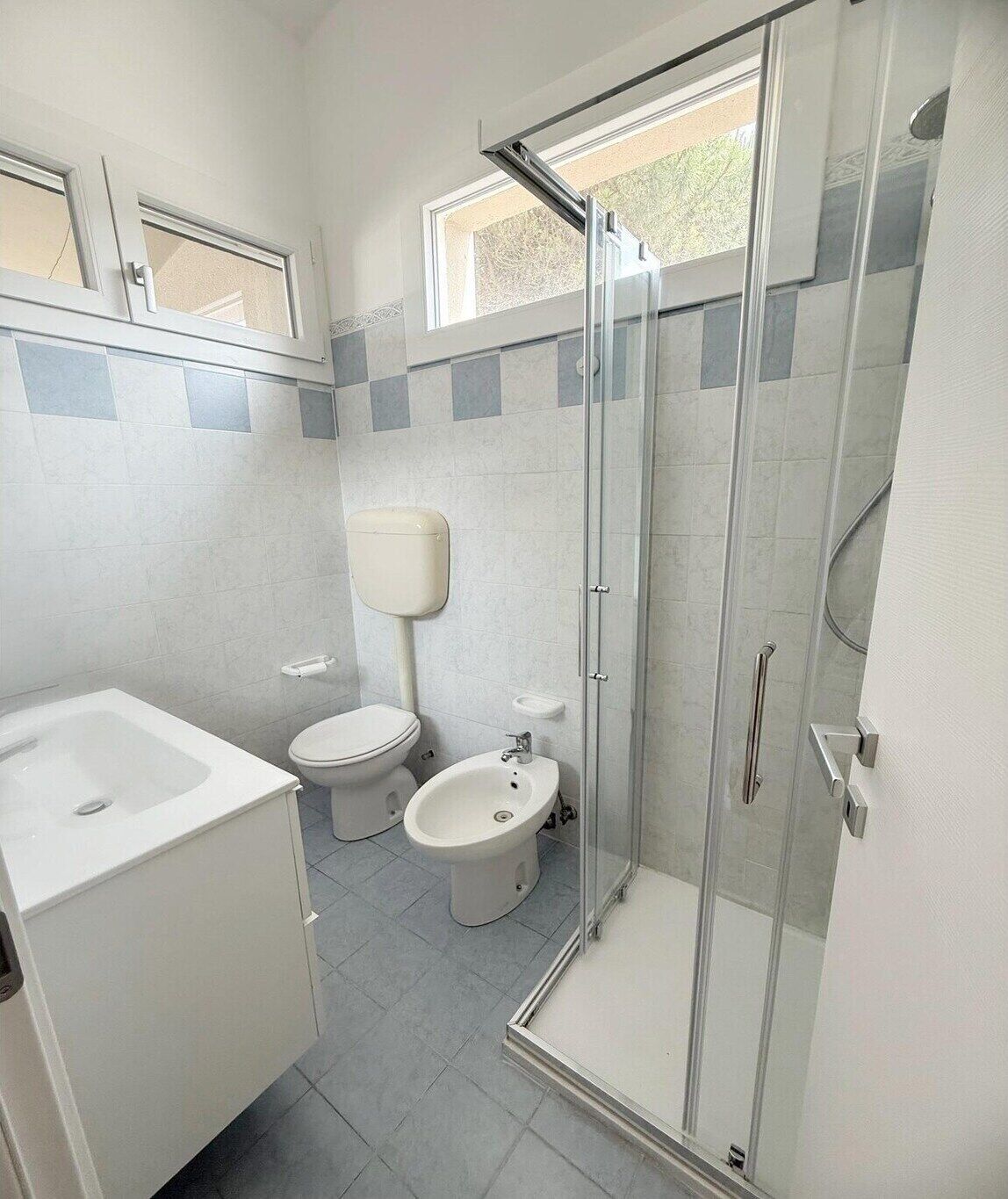 Ein Badezimmer mit einer gläsernen Duschkabine, einem Waschbecken und zwei Toiletten.