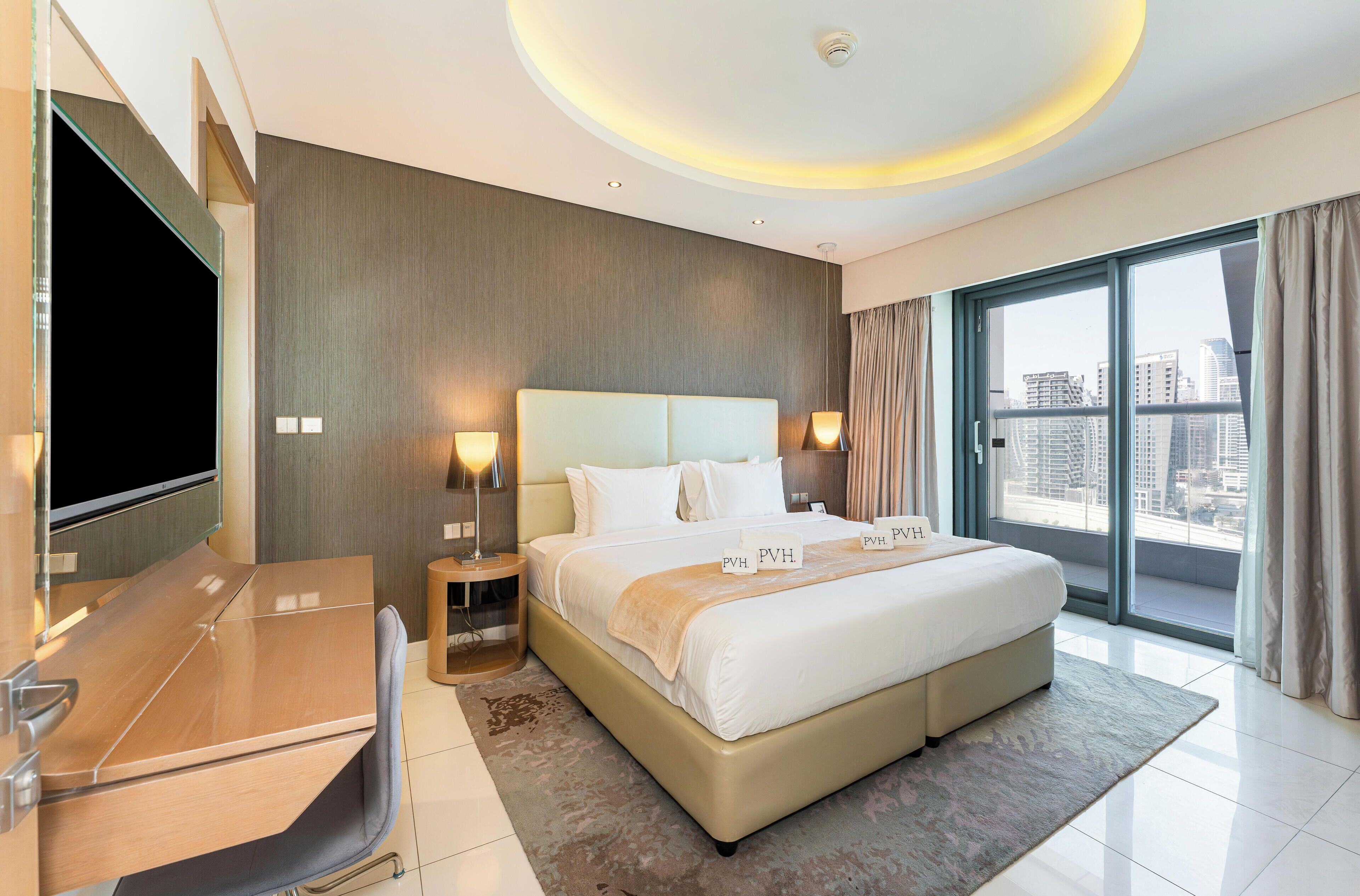 A modern hotel room with a large bed, a TV, and a city view.