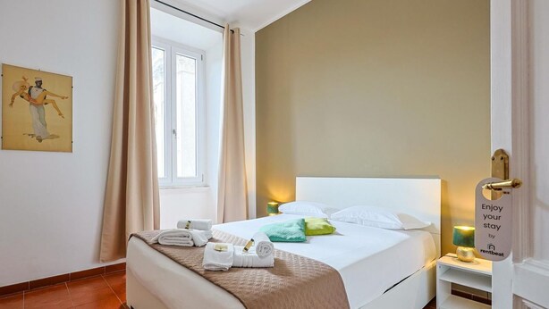 Ein Hotelzimmer mit einem Bett, einem Nachttisch, einem Fenster mit Vorhängen, einem Wandbild und einem Schild an der Tür.